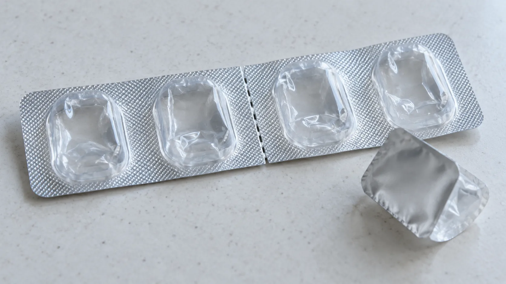 A clear blister strip split at a perforation, with one empty cavity torn free beside it